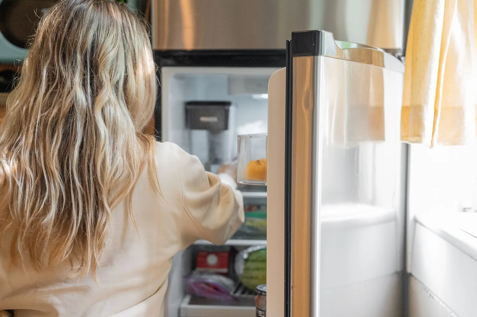 Eine Person räumt Lebensmittel in einen geöffneten Kühlschrank ein