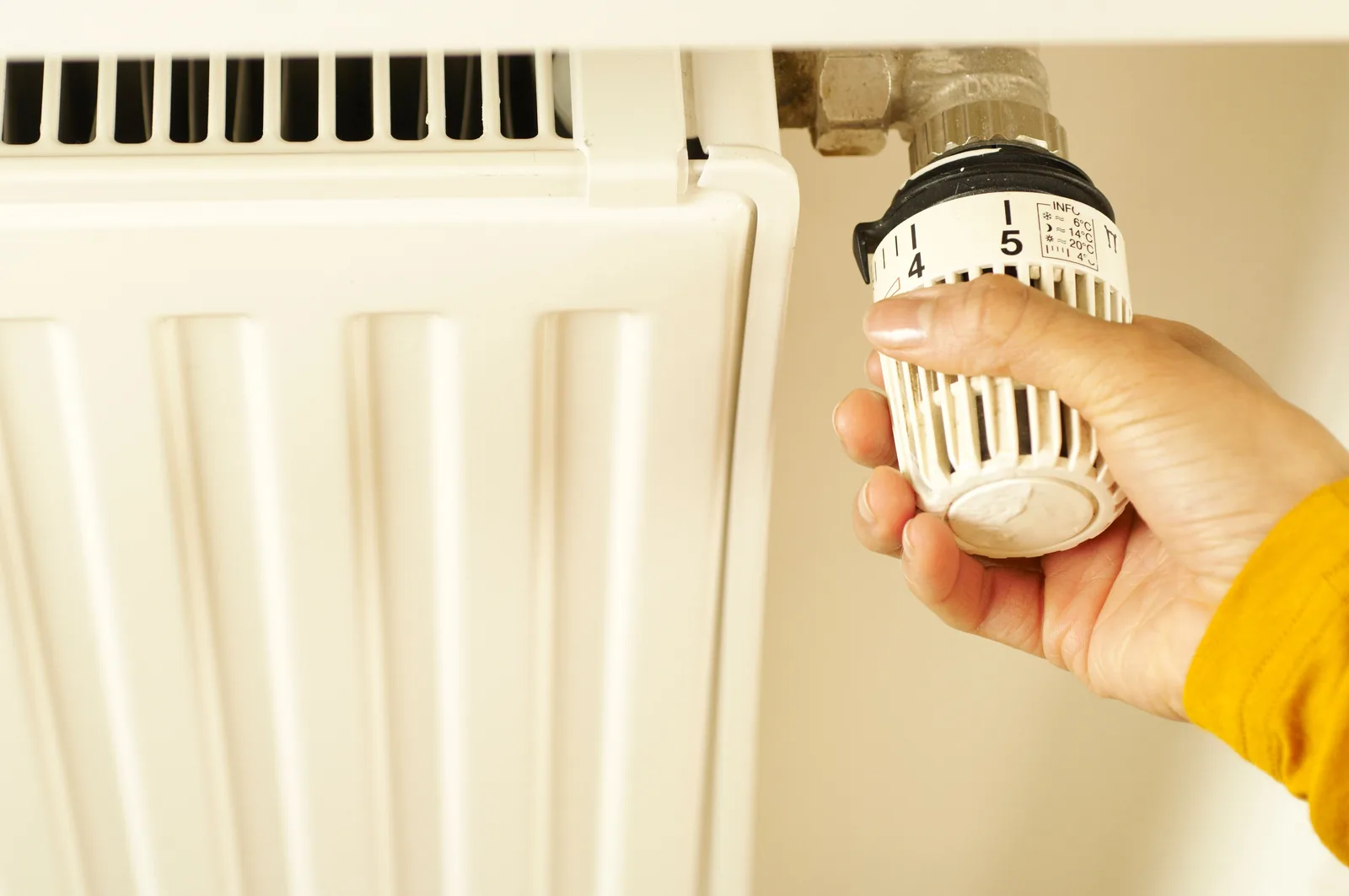 Hand stellt ein Thermostat an einem konventionellen Heizkörper ein